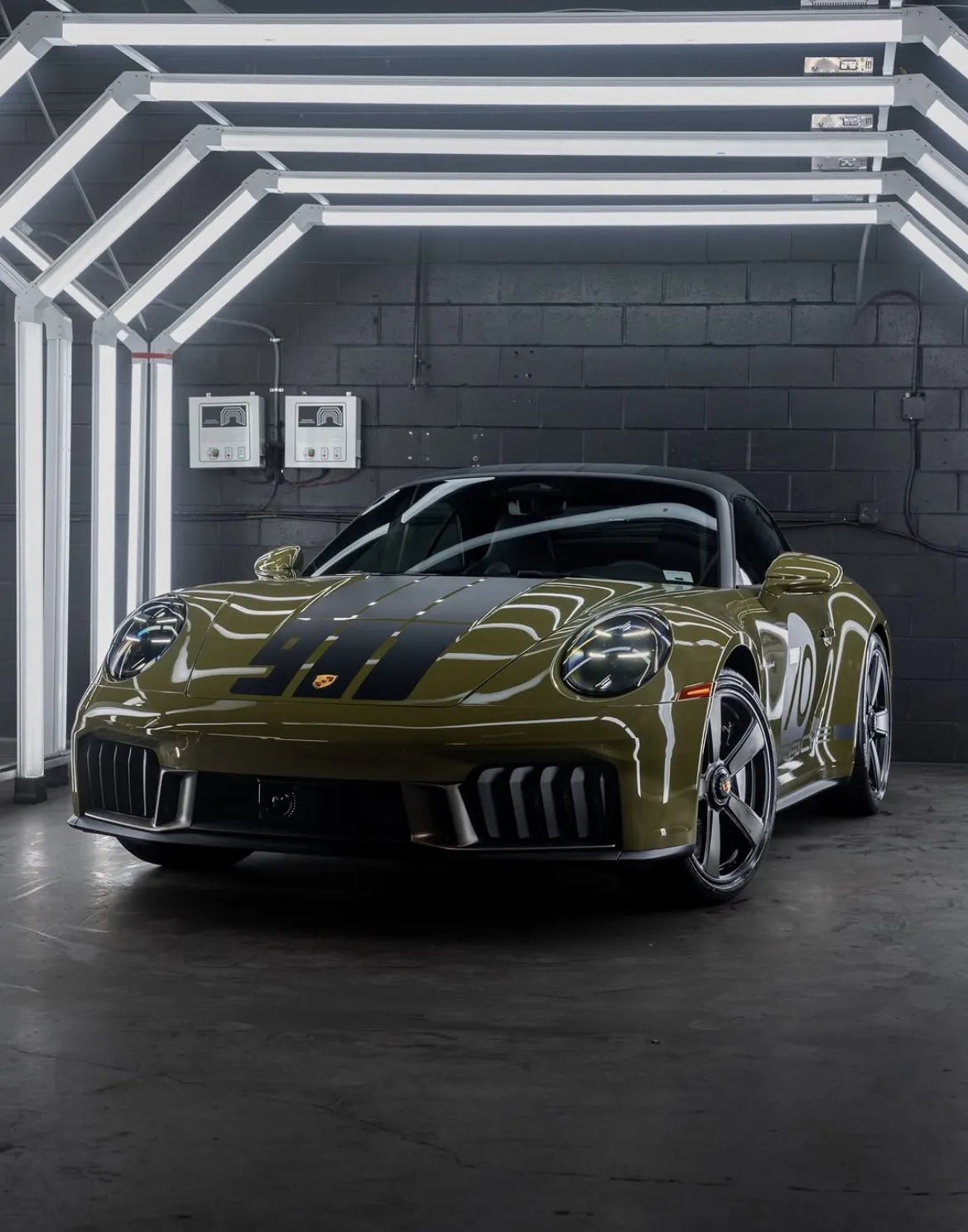 Olive Porsche with black racing stripes reflecting the detailing studio lights